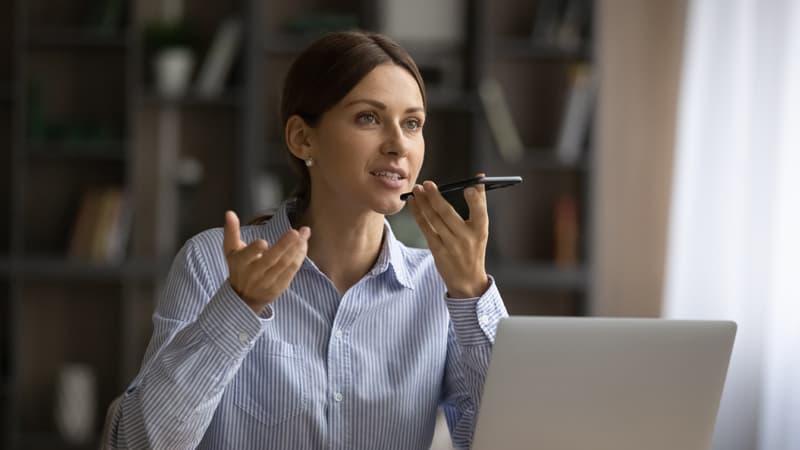Woman sitting in front of laptop and talking into speaker on phone