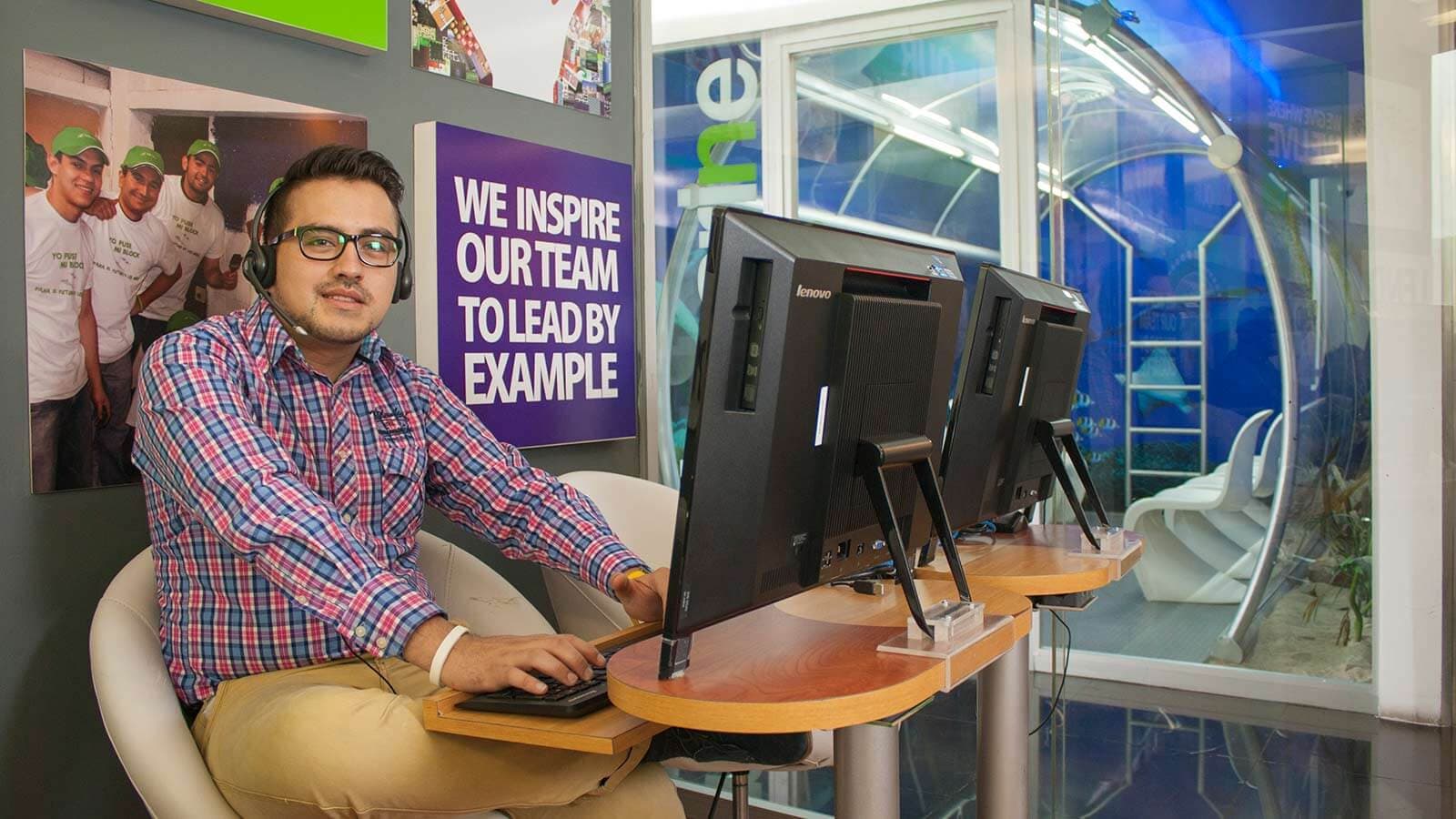 Man wearing a headset sitting in front of a computer and smiling
